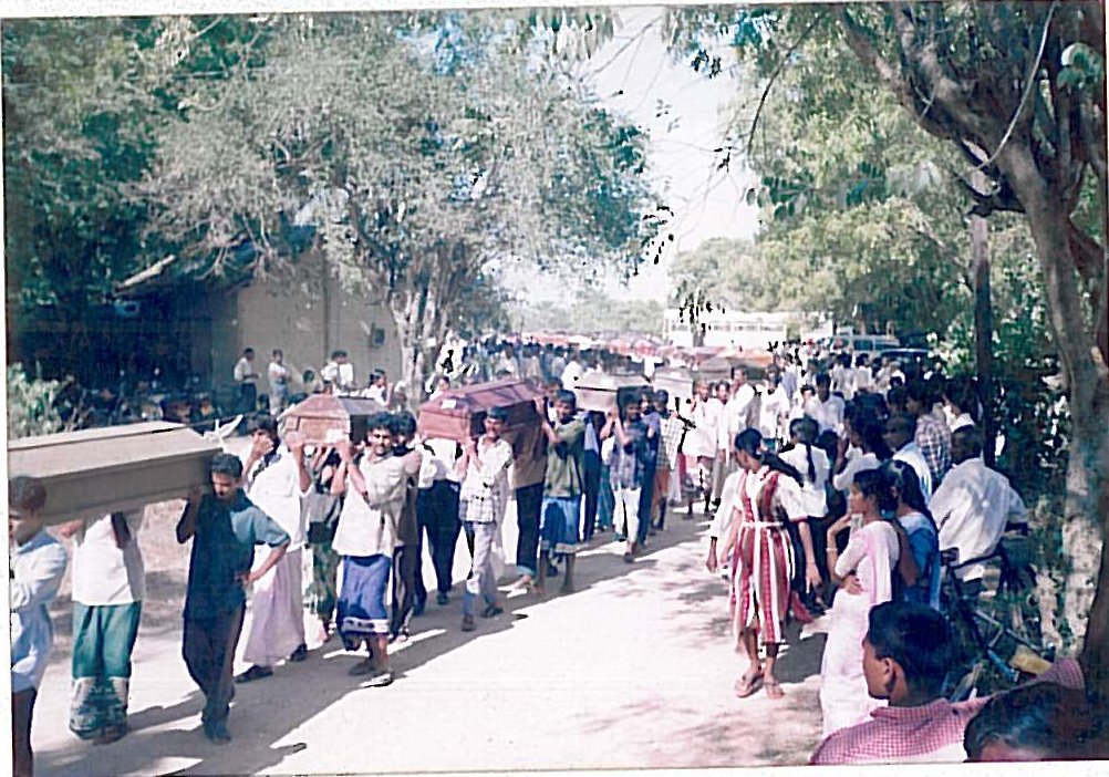 A large crowd walks along a road carrying several coffins on their shoulders